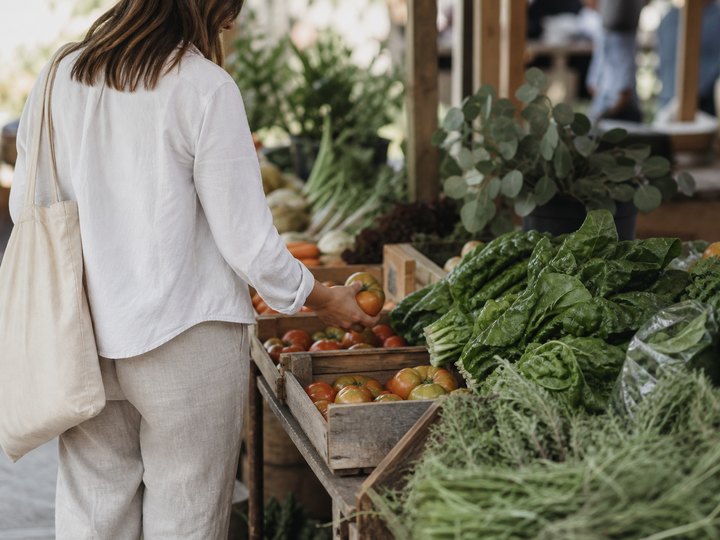 A shopper choosing seasonal tomatoes and greens at a market